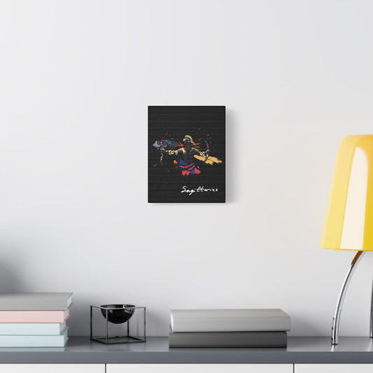 Black canvas wall art print of abstract Sagittarius archer drawing bow with dynamic warrior pose, flowing cape, and colorful splatters on dark background, featuring "Sagittarius" in elegant white cursive displayed in a modern home décor setting above a console table with books and yellow lamp.