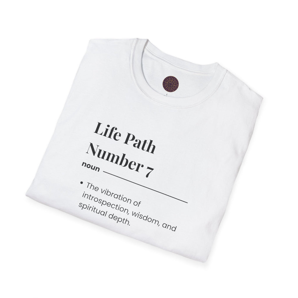 White folded unisex cotton t-shirt featuring bold Life Path Number 7 numerology print: dictionary-style definition text on introspection, wisdom, spiritual depth, and inner seeking. Motivational spiritual self-discovery crewneck tee flat lay with visible purple/gold zodiac wheel inner tag.
