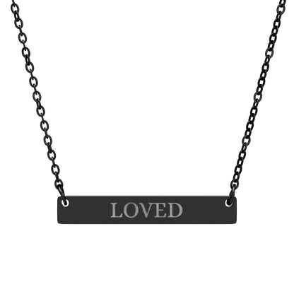 Black bar necklace with engraved uppercase text "LOVED" on a matte black pendant, suspended on a delicate black chain. Minimalist motivational affirmation jewelry for self-love, worthiness, and emotional healing.