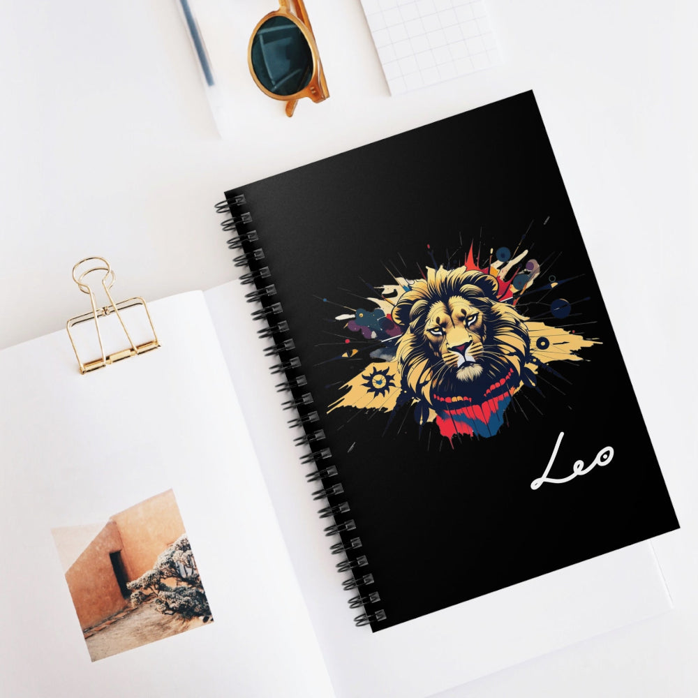Notebook with a colorful abstract lion head portrait, intense expression, flowing mane, and paint splatters on a black background, featuring the word "Leo" in elegant white cursive, placed on a minimal white desk with sunglasses and stationery items.