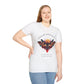 White plus-size unisex cotton t-shirt modeled by smiling woman with braided hair, hand on cheek, featuring bold "Feral" graphic on chest: vibrant abstract portrait of a fierce woman with wild flowing hair, intense expression, tribal markings, colorful geometric accents, and dynamic paint splatters in red, orange, teal, blue, and gold tones around an orange moon. White elegant cursive "Feral" text below. Wild feminine energy motivational crewneck tee.