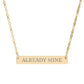 Gold bar necklace with engraved uppercase text "ALREADY MINE" on a sleek matte gold pendant, suspended on a delicate matching gold chain. Minimalist motivational affirmation jewelry for self-ownership, confidence, and empowerment.