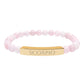 Bracelet with polished rose quartz beads in soft pink tones, natural translucent glow, paired with a gold-plated curved bar engraved "SCORPIO" in uppercase letters. Stretch-fit zodiac-inspired crystal jewelry for intensity, transformation, and emotional depth.