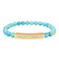 Bracelet with polished turquoise beads in soft aqua-blue tones with natural veining and speckles, featuring a gold-plated curved bar engraved "SAGITTARIUS" in uppercase letters. Stretch-fit zodiac-inspired crystal jewelry.