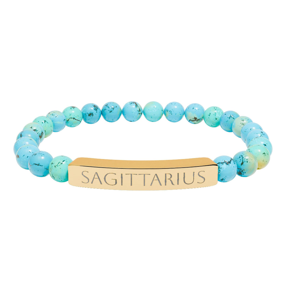 Bracelet with polished turquoise beads in soft aqua-blue tones with natural veining and speckles, featuring a gold-plated curved bar engraved "SAGITTARIUS" in uppercase letters. Stretch-fit zodiac-inspired crystal jewelry.