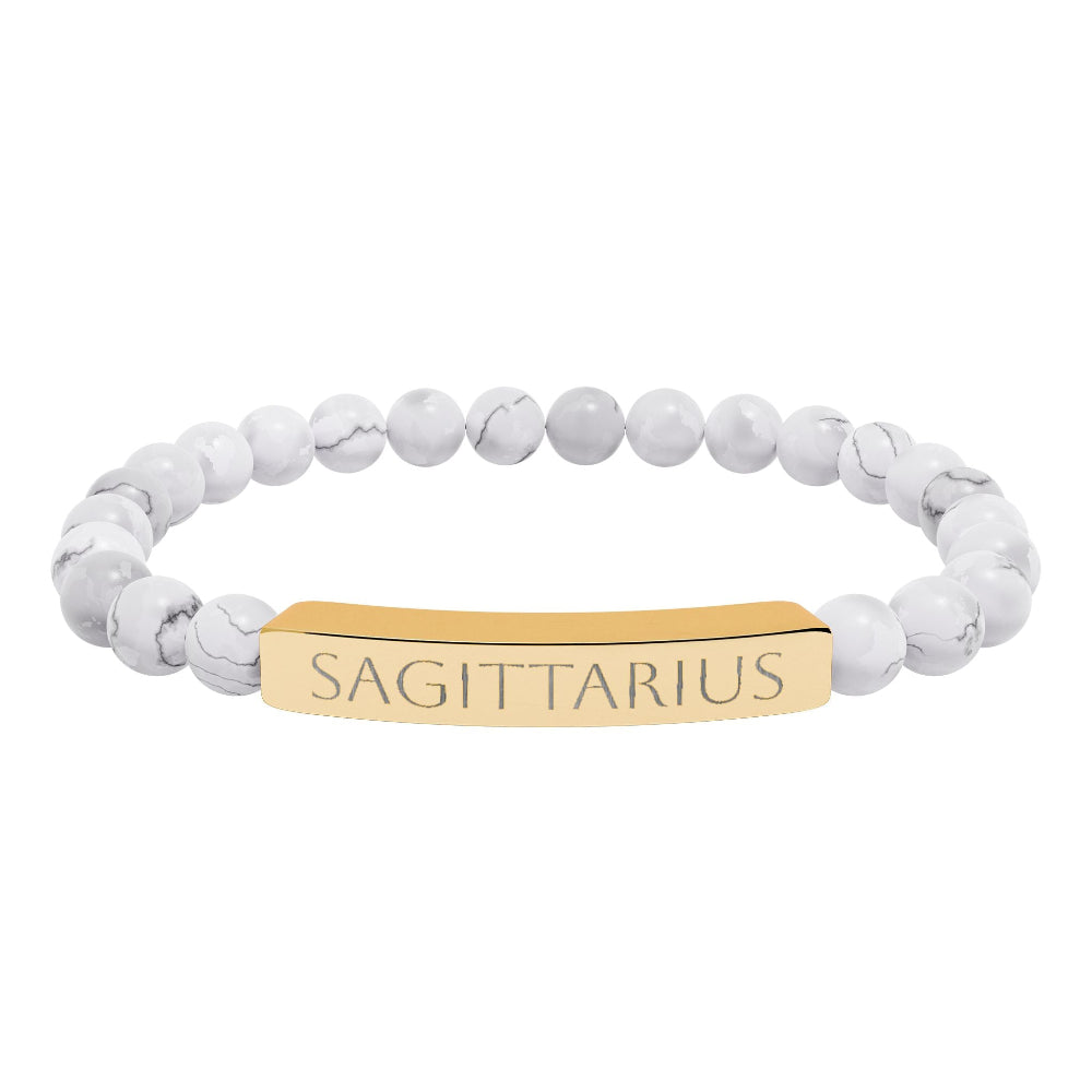 Bracelet with polished white howlite beads featuring natural gray-black veining and marbling, paired with a gold-plated curved bar engraved "SAGITTARIUS" in uppercase letters. Stretch-fit zodiac-inspired crystal jewelry.