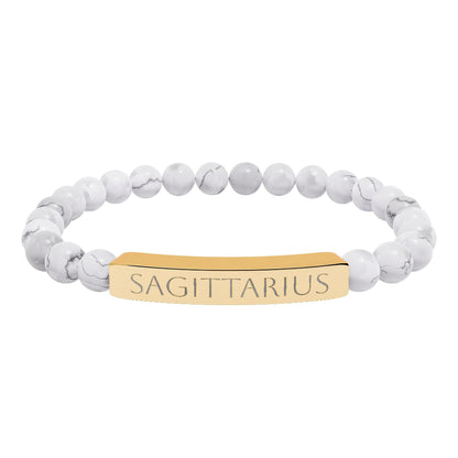 Bracelet with polished white howlite beads featuring natural gray-black veining and marbling, paired with a gold-plated curved bar engraved "SAGITTARIUS" in uppercase letters. Stretch-fit zodiac-inspired crystal jewelry.