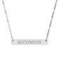 Silver bar necklace with engraved uppercase text "BECOMING" on a sleek matte silver pendant, suspended on a delicate matching silver chain. Minimalist motivational affirmation jewelry for growth, transformation, and self-evolution.