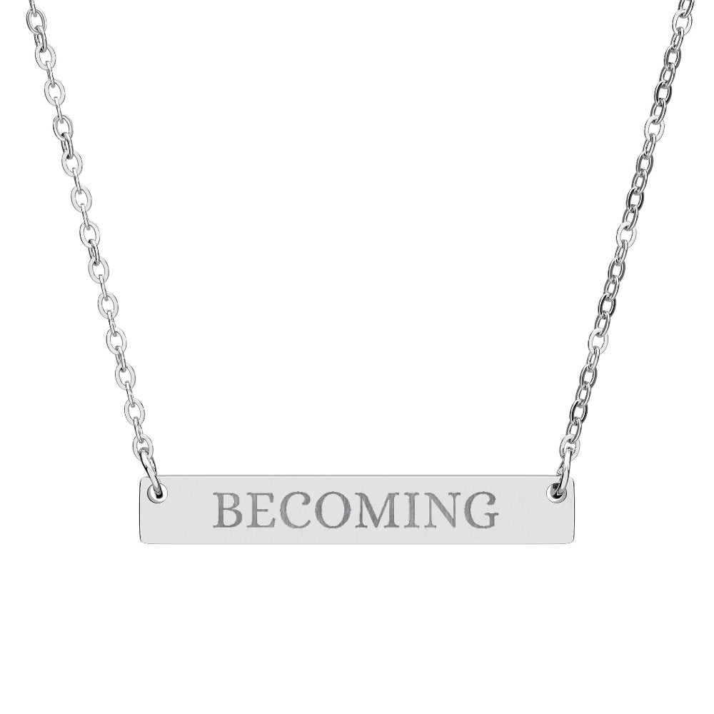 Silver bar necklace with engraved uppercase text "BECOMING" on a sleek matte silver pendant, suspended on a delicate matching silver chain. Minimalist motivational affirmation jewelry for growth, transformation, and self-evolution.