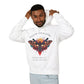 Young man with short hair pulling up the hood of a white hoodie featuring vibrant multicolored moth/butterfly graphic, geometric sun/moon elements, "FOLLOW YOUR LIGHT" arched text above, motivational quote "Even when others can't see where you're going" below