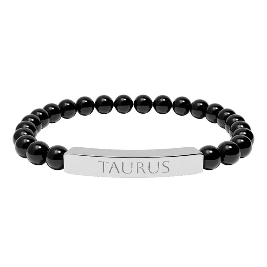 Bracelet with polished black onyx beads and silver curved bar engraved "TAURUS" in uppercase letters. Stretch-fit zodiac-inspired crystal jewelry.