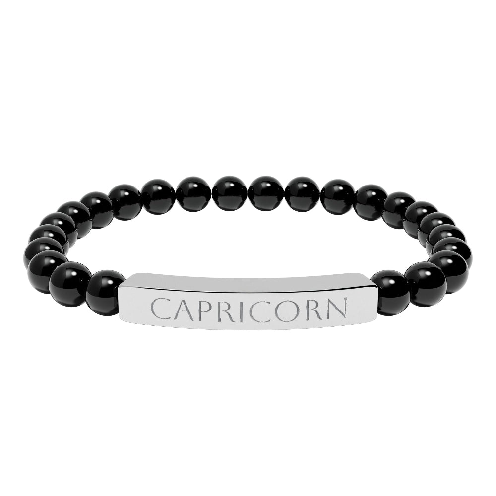Bracelet with polished black onyx beads and silver curved bar engraved "CAPRICORN" in uppercase letters. Stretch-fit zodiac-inspired crystal jewelry.