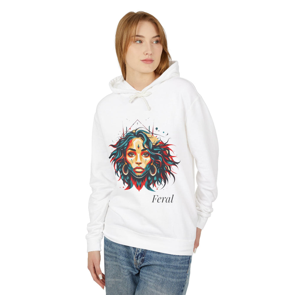 Young woman with long hair modeling white hoodie featuring vibrant artistic portrait of a fierce woman with curly multicolored flowing hair, teal red blue face accents, large hoop earrings, third-eye symbol, geometric backdrop, "Feral" text below