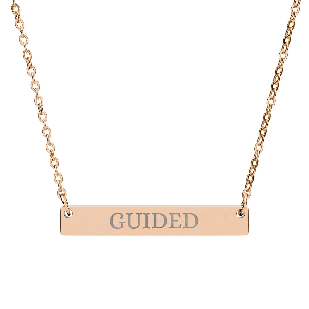 Rose gold bar necklace with engraved uppercase text "GUIDED" on a sleek matte pendant, suspended on a delicate matching rose gold chain. Minimalist motivational affirmation jewelry for guidance, intuition, and spiritual alignment.