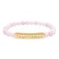 Bracelet with polished rose quartz beads in soft pink tones, natural translucent glow, paired with a gold-plated curved bar engraved "SAGITTARIUS" in uppercase letters. Stretch-fit zodiac-inspired crystal jewelry.