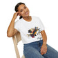 White unisex cotton t-shirt modeled by smiling woman with braided hair, seated pose, hand on cheek, featuring bold Virgo zodiac graphic on chest: vibrant abstract woman holding wheat sheaf, serene expression, flowing hair with headscarf, detailed feathers, geometric accents, and dynamic multicolored paint splatters in gold, red, navy, teal, and black tones bursting outward. Elegant black cursive "Virgo" text below. Astrology zodiac motivational crewneck tee.