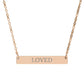 Rose gold bar necklace with engraved uppercase text "LOVED" on a sleek matte pendant, suspended on a delicate matching rose gold chain. Minimalist motivational affirmation jewelry for self-love, worthiness, and emotional healing.