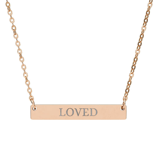 Rose gold bar necklace with engraved uppercase text "LOVED" on a sleek matte pendant, suspended on a delicate matching rose gold chain. Minimalist motivational affirmation jewelry for self-love, worthiness, and emotional healing.