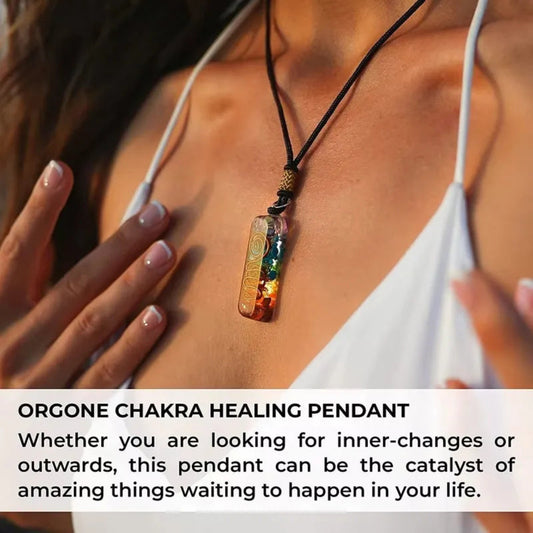 Model wearing orgone chakra healing pendant necklace – rectangular clear resin with layered rainbow gemstones (red jasper, carnelian, citrine, green aventurine, lapis, amethyst) and copper spiral for energy balancing, gold engraved bail on black cord, sunlit skin close-up