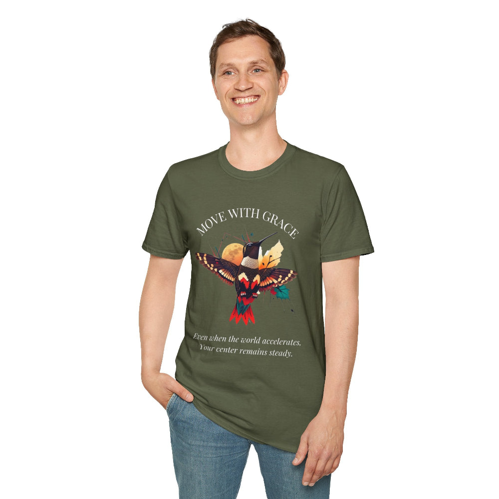 Man wearing a olive green speckled t-shirt featuring a vibrant hummingbird graphic with the text "MOVE WITH GRACE" above and the quote "Even when the world accelerates, Your center remains steady" below. Casual motivational streetwear style with blue jeans.