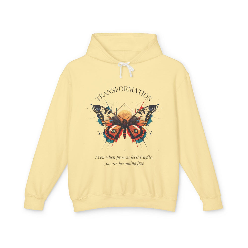 Light yellow hoodie featuring colorful abstract butterfly graphic with moon background, "TRANSFORMATION" arched above, and inspirational quote "Even when process feels fragile, you are becoming free" below
