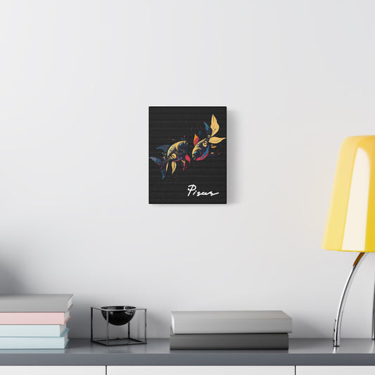 Black canvas wall art print of colorful abstract mirrored fish with flowing fins and cosmic splatters on dark background, featuring "Pisces" in elegant white cursive displayed in a modern home décor setting above a console table with books and yellow lamp.