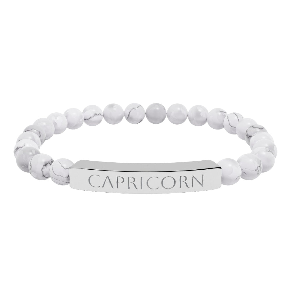 Bracelet with polished white howlite beads featuring natural gray-black veining and marbling, paired with a silver curved bar engraved "CAPRICORN" in uppercase letters. Stretch-fit zodiac-inspired crystal jewelry.