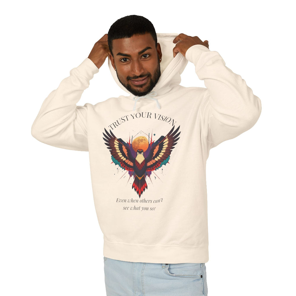 Young man modeling cream hoodie with colorful abstract eagle/phoenix graphic, "TRUST YOUR VISION" arched above, and inspirational quote "Even when others can't see what you see" below, pulling up hood