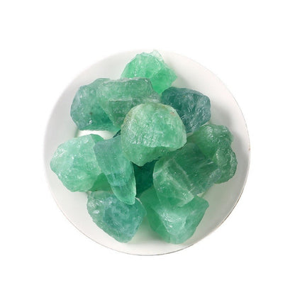 Close-up of raw green fluorite crystals: cluster of translucent emerald-green rough stones with natural cubic shapes, glassy luster, and subtle internal clarity, displayed in a white bowl on a light background. Natural healing gemstone for heart chakra, emotional balance, and mental clarity.