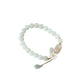 Pale green jade beaded bracelet with translucent pink agate focal bead, gold plum blossom charm, and dangling jade-amethyst teardrop pendants flat lay