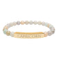 Bracelet with polished pastel beads in soft peach, cream, gray, and light blue tones with natural marbling, featuring a gold-plated curved bar engraved "CAPRICORN" in uppercase letters. Stretch-fit zodiac-inspired crystal jewelry.