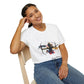 White unisex cotton t-shirt modeled by smiling woman with braided hair, seated pose, hand on cheek, featuring bold Sagittarius zodiac graphic: vibrant abstract archer silhouette drawing bow, dynamic warrior pose with flowing cape, intricate armor details, and explosive multicolored paint splatters in gold, red, navy, teal, and black tones bursting outward. Elegant black cursive "Sagittarius" text below. Astrology zodiac motivational crewneck tee.