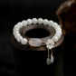 White jade beaded bracelet with translucent agate focal bead, gold plum blossom charm, and dangling jade & amethyst drops on wooden stand