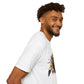 White unisex cotton t-shirt in side profile on smiling male model with curly hair and beard, featuring bold Year of the Goat zodiac graphic on chest: vibrant abstract goat / ram head portrait with large curved horns, intense glowing eyes, geometric diamond accents, flowing beard details, and dynamic multicolored paint splatters in gold, red, blue, teal, orange, and black tones exploding outward. Chinese text "羊年" (Year of the Goat) printed below in black. Zodiac Chinese New Year motivational crewneck tee.