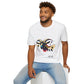White unisex cotton t-shirt modeled by smiling man with curly hair and beard, seated pose, featuring bold Year of the Goat graphic: vibrant abstract goat head portrait with large curved horns, intense expression, geometric patterns, and dynamic multicolored paint splatters in gold, red, black, blue, teal, and orange tones exploding outward. Chinese text "羊年" (Year of the Goat) printed below in black. Zodiac Chinese New Year motivational crewneck tee.
