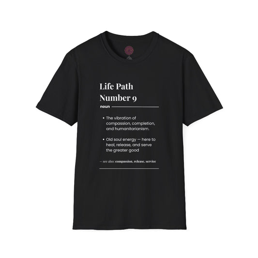 Black unisex cotton t-shirt laid out flat featuring bold Life Path Number 9 numerology print in dictionary style: exact text reading "Life Path Number 9 noun · The vibration of compassion, completion, and humanitarianism. · Old soul energy — here to heal, release, and serve the greater good. – see also: compassion, release, service". Motivational spiritual numerology crewneck tee flat lay with visible purple/gold zodiac wheel inner tag.