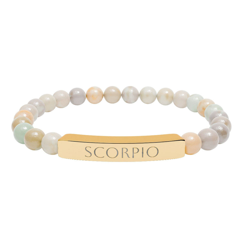Bracelet with polished round beads in soft pastel tones (cream, peach, gray, light blue, and gold flecks) with natural marbling, featuring a gold-plated curved bar engraved "SCORPIO" in uppercase letters. Stretch-fit zodiac-inspired crystal jewelry for intensity, transformation, and emotional depth.