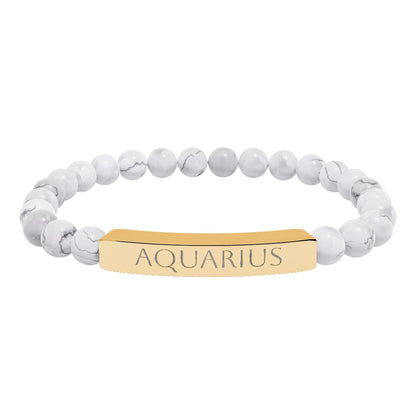 Bracelet with polished white howlite beads featuring natural gray-black veining and marbling, paired with a gold-plated curved bar engraved "AQUARIUS" in uppercase letters. Stretch-fit zodiac-inspired crystal jewelry.