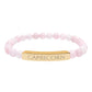 Bracelet with polished rose quartz beads in soft pink tones, natural translucent glow, paired with a gold-plated curved bar engraved "CAPRICORN" in uppercase letters. Stretch-fit zodiac-inspired crystal jewelry for ambition, discipline, and grounding.
