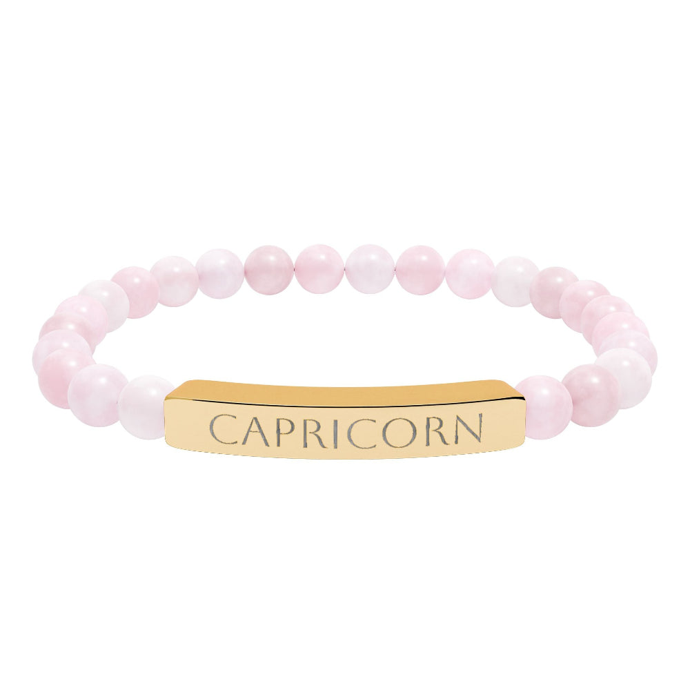 Bracelet with polished rose quartz beads in soft pink tones, natural translucent glow, paired with a gold-plated curved bar engraved "CAPRICORN" in uppercase letters. Stretch-fit zodiac-inspired crystal jewelry for ambition, discipline, and grounding.