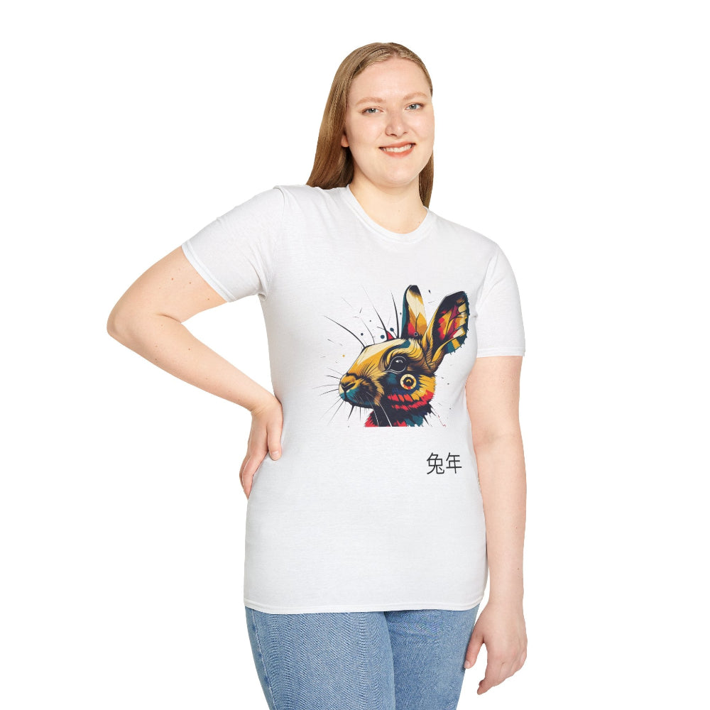 White unisex cotton t-shirt modeled by smiling plus-size female with long blonde hair, hand on hip, featuring bold Year of the Rabbit graphic: vibrant abstract rabbit face portrait with large expressive ears, intense glowing eyes, geometric patterns, and dynamic multicolored paint splatters in gold, red, blue, teal, orange, and black tones exploding outward. Chinese text "兔年" (Year of the Rabbit) printed below in black. Zodiac Chinese New Year motivational crewneck tee.