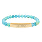 Bracelet with polished turquoise beads in soft aqua-blue tones with natural veining and speckles, featuring a gold-plated curved bar engraved "GEMINI" in uppercase letters. Stretch-fit zodiac-inspired crystal jewelry.