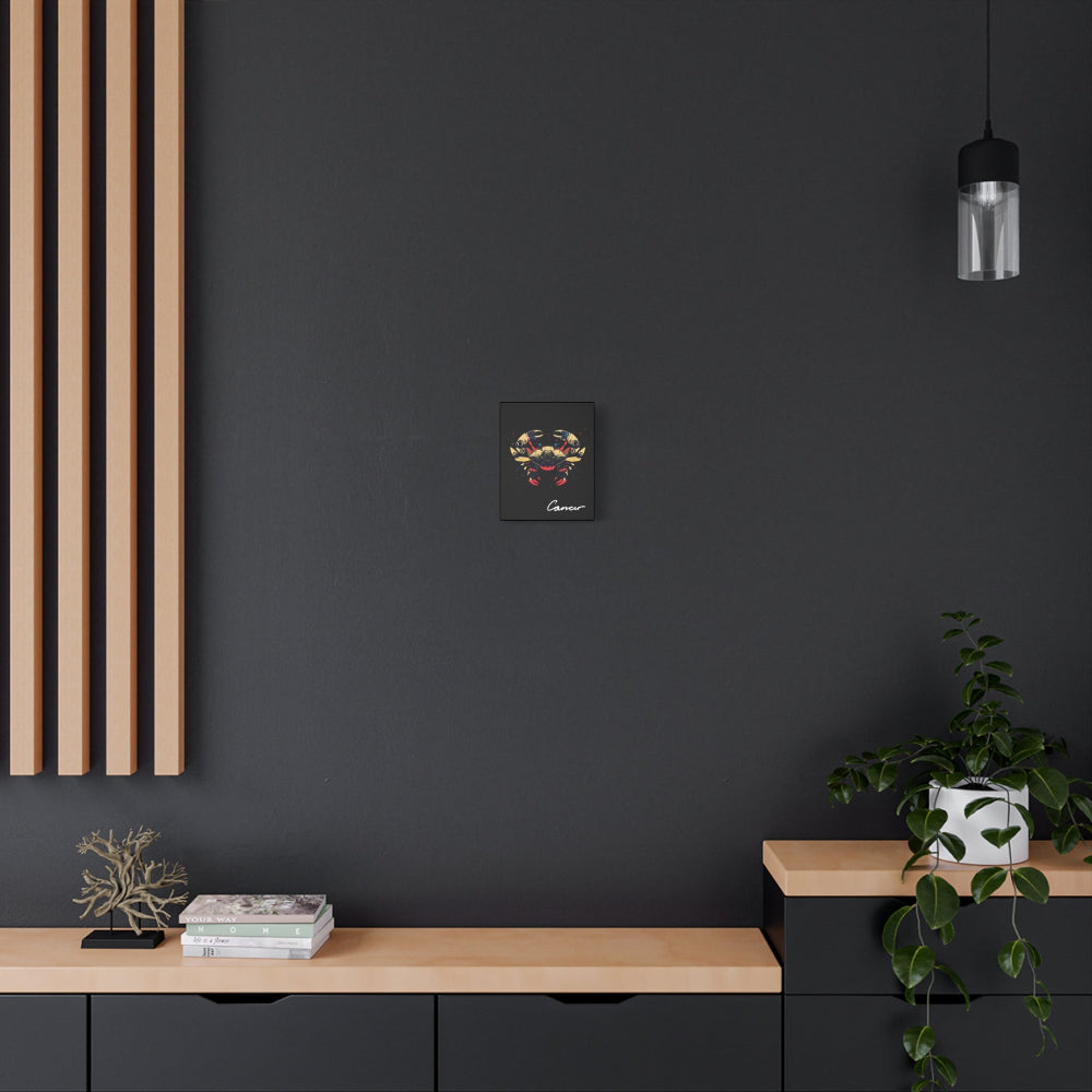 Black canvas wall art print of colorful abstract Cancer crab illustration with intricate details and cosmic splatters on dark background, featuring "Cancer" in elegant white cursive hung on a dark grey wall above a wooden shelf with potted plants.
