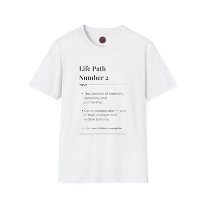 White folded unisex cotton t-shirt featuring bold Life Path Number 2 numerology print in dictionary style: exact text reading "Life Path Number 2 noun · The vibration of harmony, sensitivity, and partnership. · Gentle collaborator — here to heal, connect, and restore balance. – see also: peace, balance, connection". Motivational spiritual numerology crewneck tee flat lay with visible purple/gold zodiac wheel inner tag.