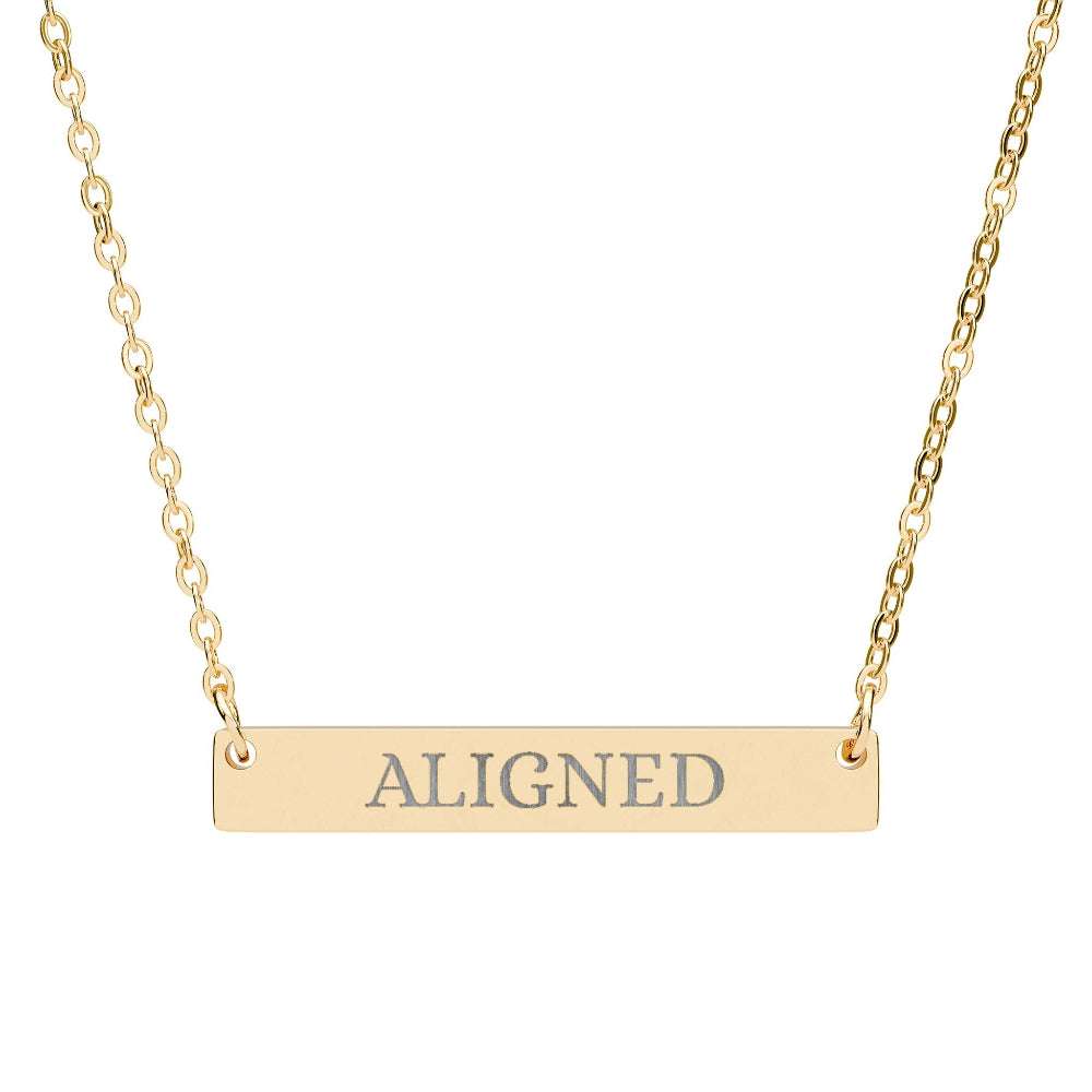 Gold bar necklace with engraved uppercase text "ALIGNED" on a sleek matte pendant, suspended on a delicate matching gold chain. Minimalist motivational affirmation jewelry for alignment, balance, and spiritual harmony.