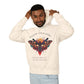 Young man with short hair pulling up the hood of a cream hoodie featuring vibrant multicolored moth/butterfly graphic, geometric sun/moon elements, "FOLLOW YOUR LIGHT" arched text above, motivational quote "Even when others can't see where you're going" below