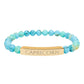 Bracelet with turquoise beaded stretch strand in soft aqua-blue tones with natural veining and speckles, featuring a gold-plated curved bar engraved "CAPRICORN" in uppercase letters. Zodiac-inspired healing crystal jewelry for ambition, discipline, and grounding.