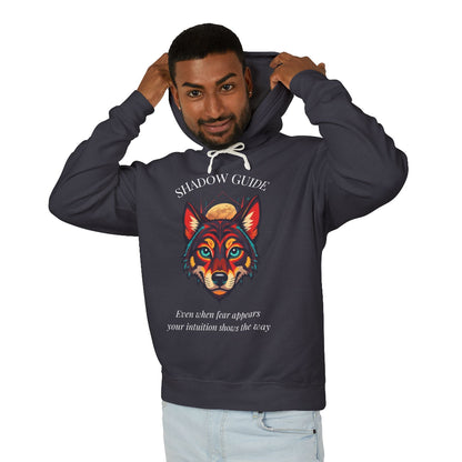 Young man with short hair pulling up the hood of a dark gray hoodie featuring vibrant multicolored wolf head graphic, intense eyes in orange blue teal splashes, full moon above, "SHADOW GUIDE" arched text, motivational quote about intuition and fear below