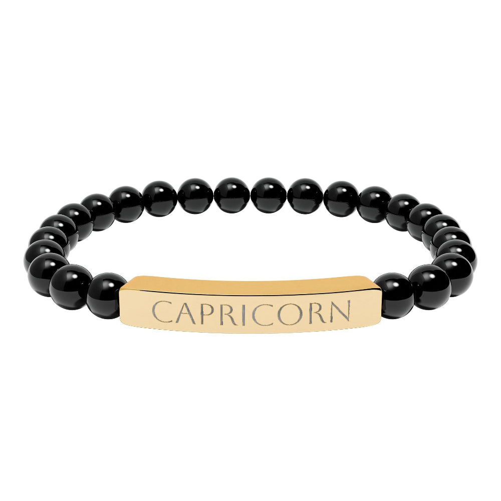 Black beaded bracelet featuring polished round black onyx or obsidian beads with a gold-plated curved bar engraved "CAPRICORN" in uppercase letters. Stretch-fit zodiac-inspired jewelry for grounding,