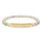 Bracelet with polished pastel beads in soft peach, cream, gray, and light blue tones with natural marbling, featuring a gold-plated curved bar engraved "SAGITTARIUS" in uppercase letters. Stretch-fit zodiac-inspired crystal jewelry.